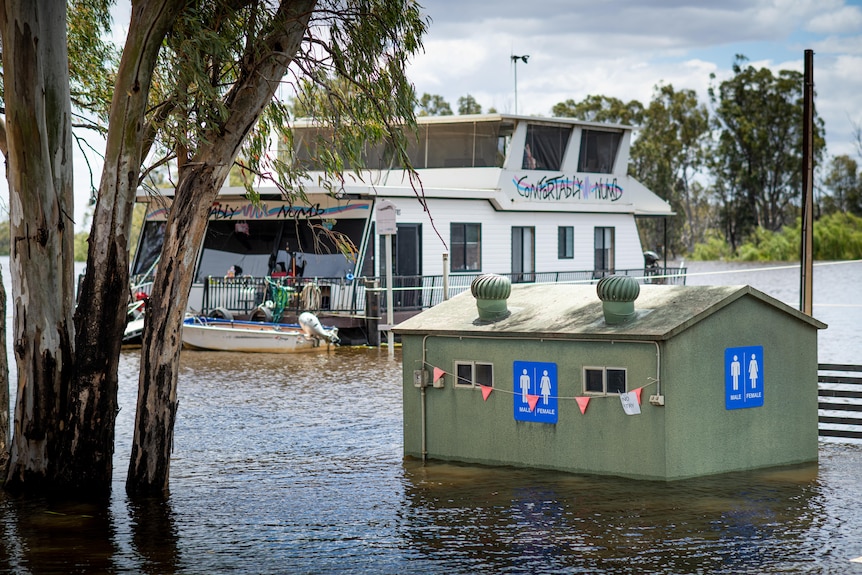 A houseboat on the river next to a toilet block surrounded by water