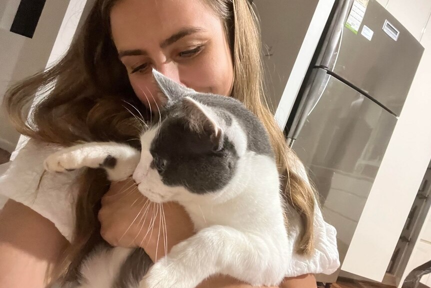 A woman cuddling a white and grey cat.