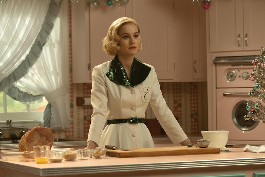 La actriz Brie Larson con un peinado de los años 50 y un vestido verde y blanco brillante está en una cocina en el programa Lessons in Chemistry.