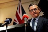 Michael Gunner looks across the camera while standing at a lectern in front of an Australian flag.