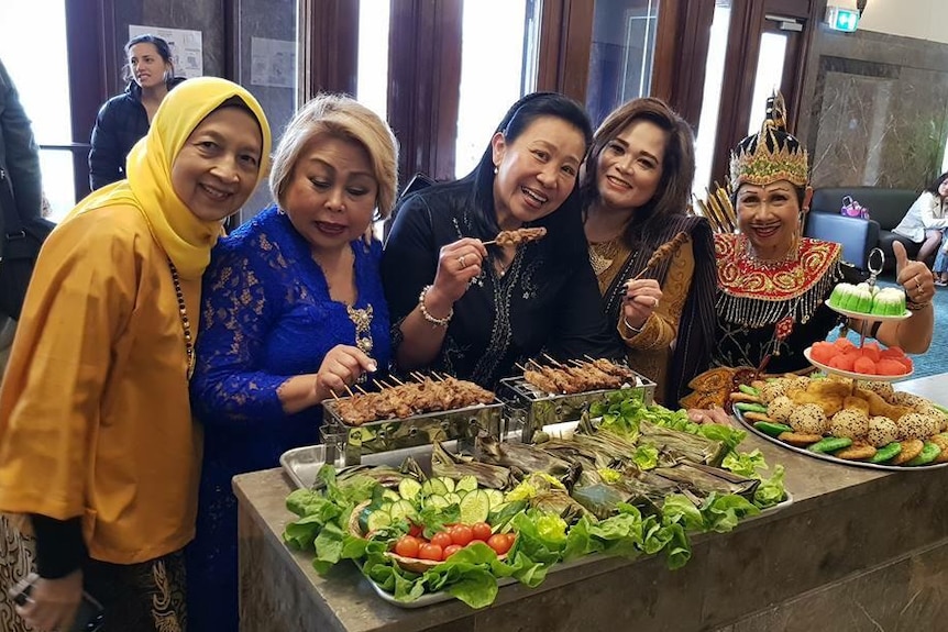 A group of woman smiling with various of food in front of them