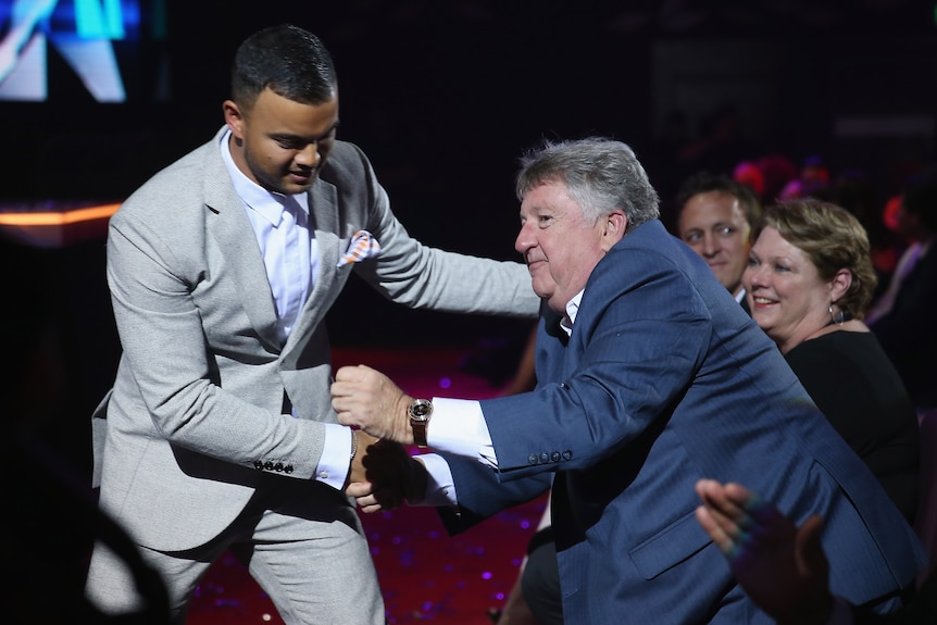 Denis Handlin stands and leans forward to shake the hand of Guy Sebastian at an awards ceremony.