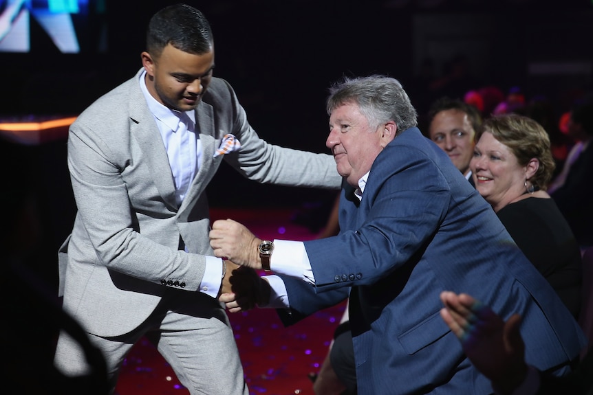 Denis Handlin stands and leans forward to shake the hand of Guy Sebastian at an awards ceremony.