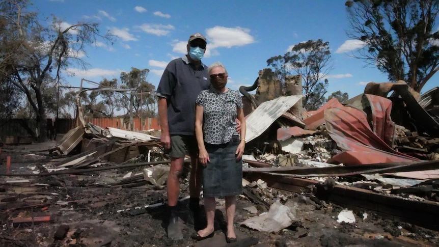 Two people standing in front of a burned down shed. 