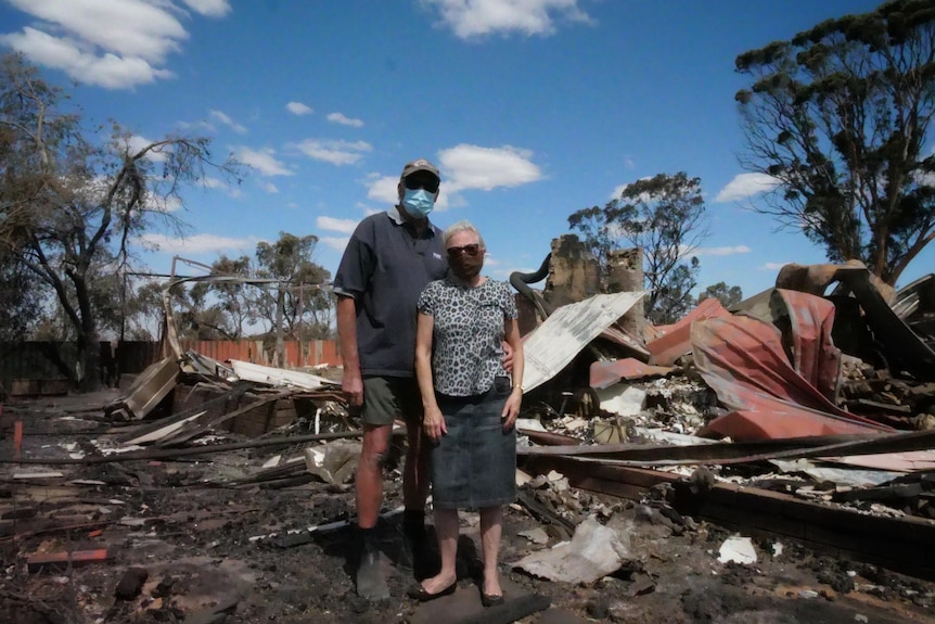 Two people standing in front of a burned down shed. 