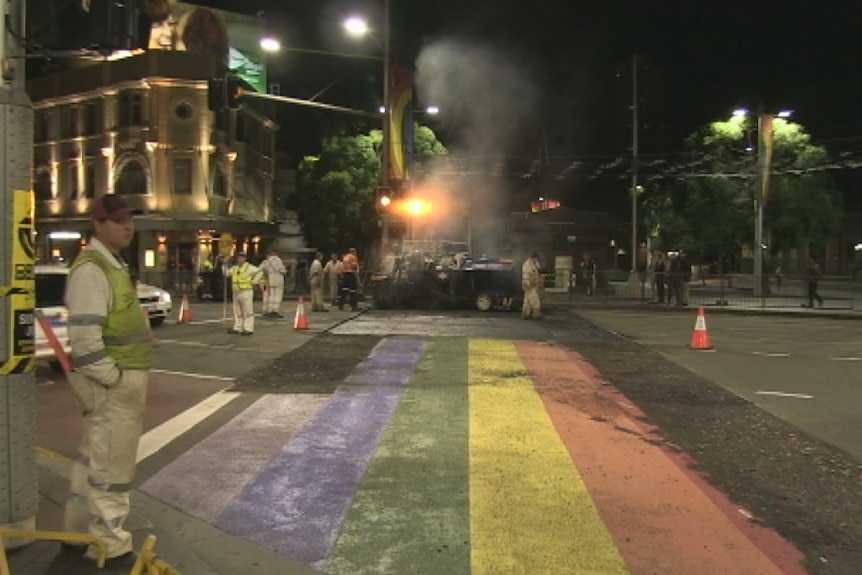 Rainbow crossing being covered in asphalt at night time.