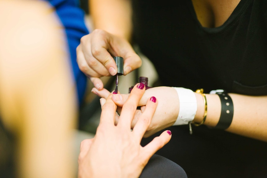 A person puts nail polish on another person's finger nails.