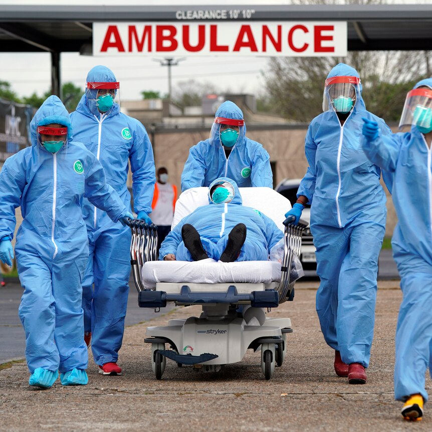 People in protective equipment and masks transport a patient on a stretcher from an ambulance