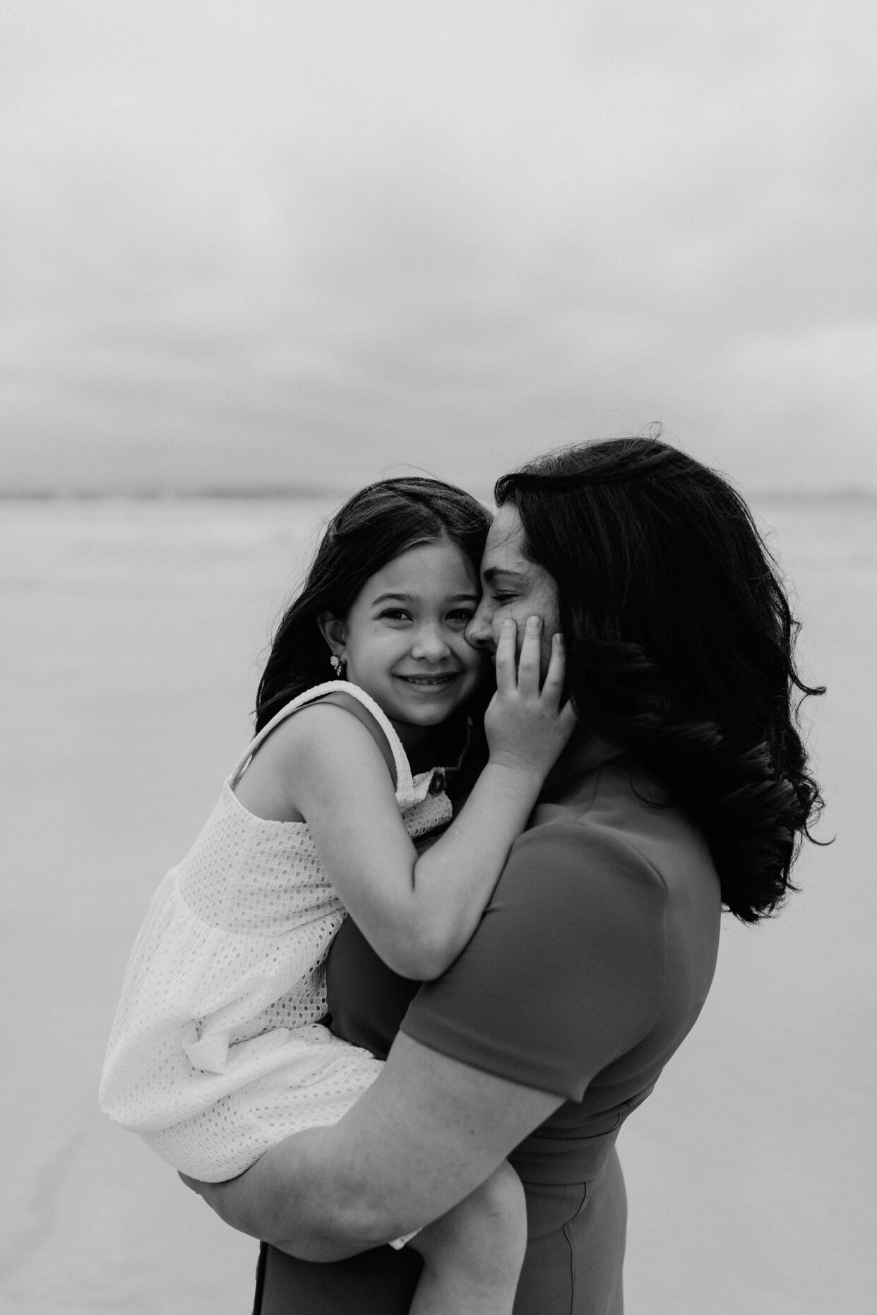 A woman embraces her daughter on the beach. 