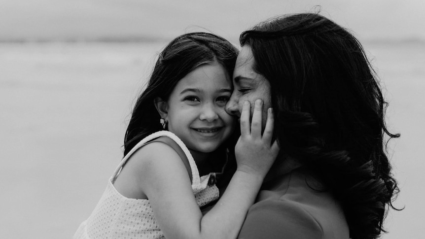 A woman embraces her daughter on the beach. 