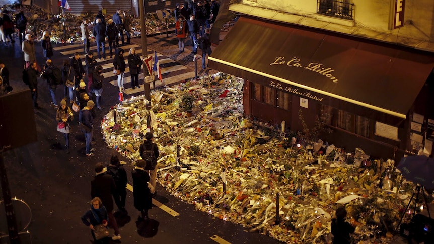 A view from above Le Carillon restaurant at night where people have gathered and placed many bouquets of flowers.