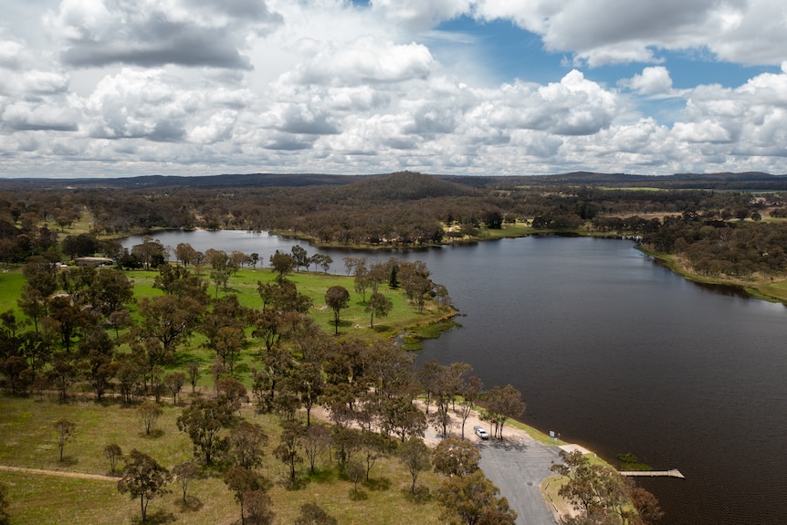 a large dam full of water is surrounded by green grass, trees and a road