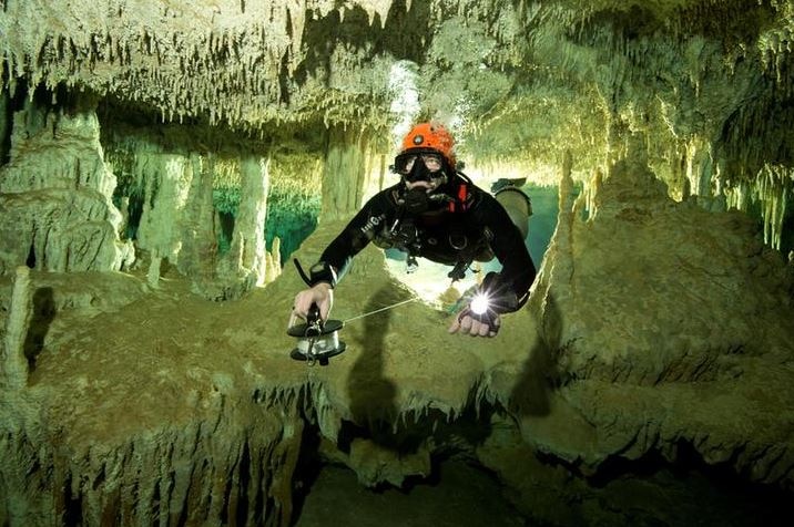 A diver measures the length of the Sac Actun underwater cave system, lit up with a torch.