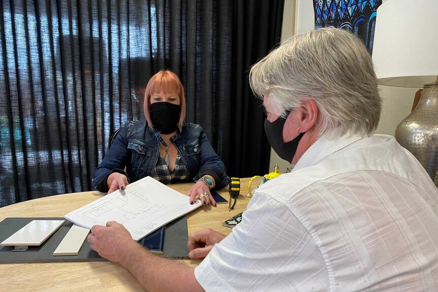 A woman sitting behind a desk shows plans to a customer