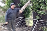 Farmer Warren Salway standing next to burnt trees with a chainsaw.