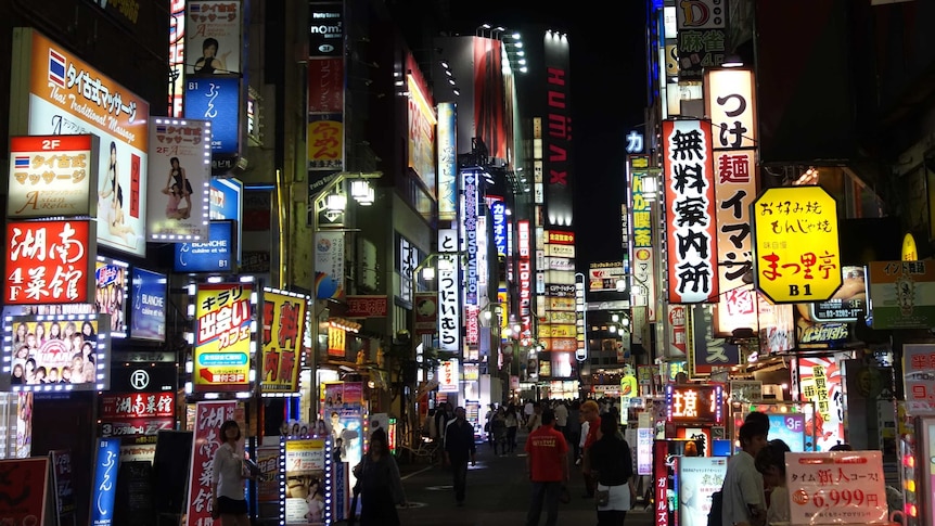 Numerous shop signs illuminate a crowded street.