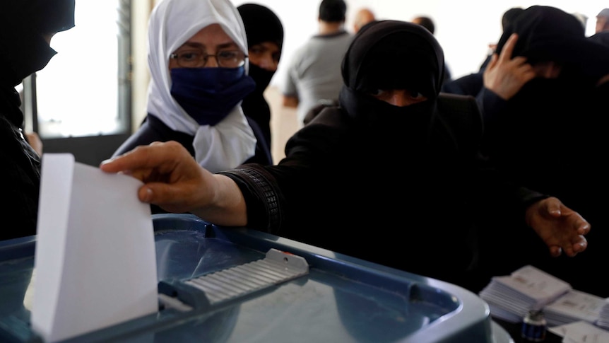 A woman in a niqab puts an envelope in a plastic box.