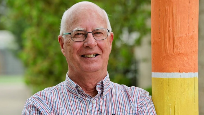 Smiling man with glasses leaning against pole