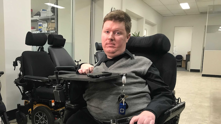 Mark Brown sits in his wheelchair looking towards the camera, in the background there are other empty wheelchairs