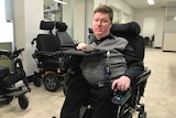 Mark Brown sits in his wheelchair looking towards the camera, in the background there are other empty wheelchairs