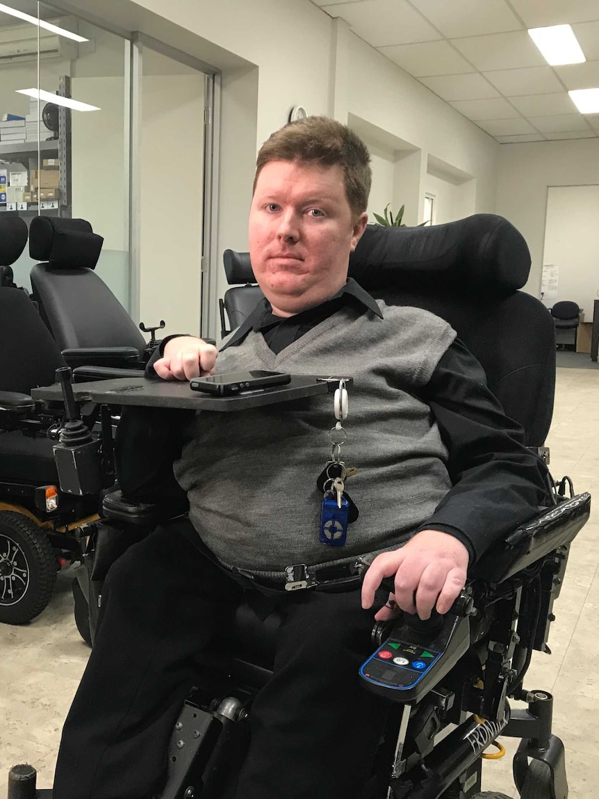 Mark Brown sits in his wheelchair looking towards the camera, in the background there are other empty wheelchairs