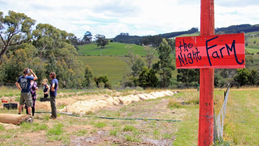Red sign saying night farm with rolling green hills behind it