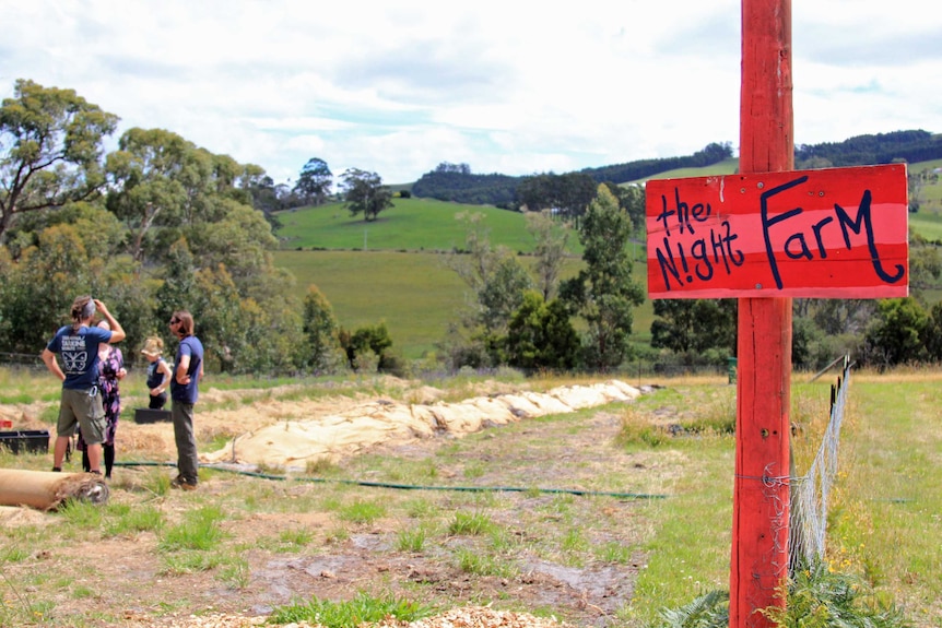 Red sign saying night farm with rolling green hills behind it