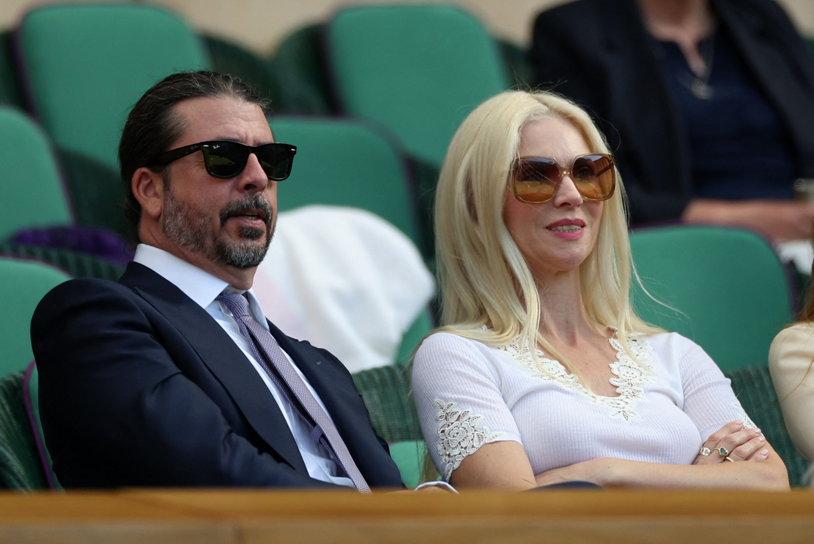 Musician Dave Grohl in a dark suit and sunglasses with his wife actress Jordyn Blum in a white lace trim dress 