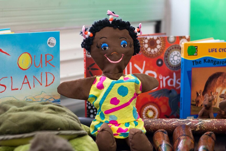 A close up of a doll with children's books in the background.