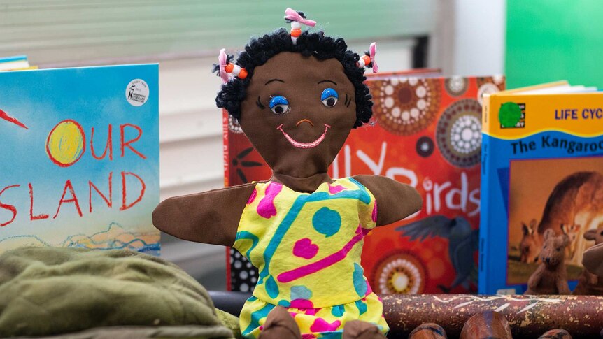 A close up of a doll with children's books in the background.