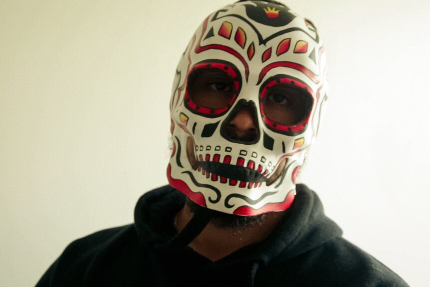 A man wearing a Mexican day of the dead style mask and a black hoodie.