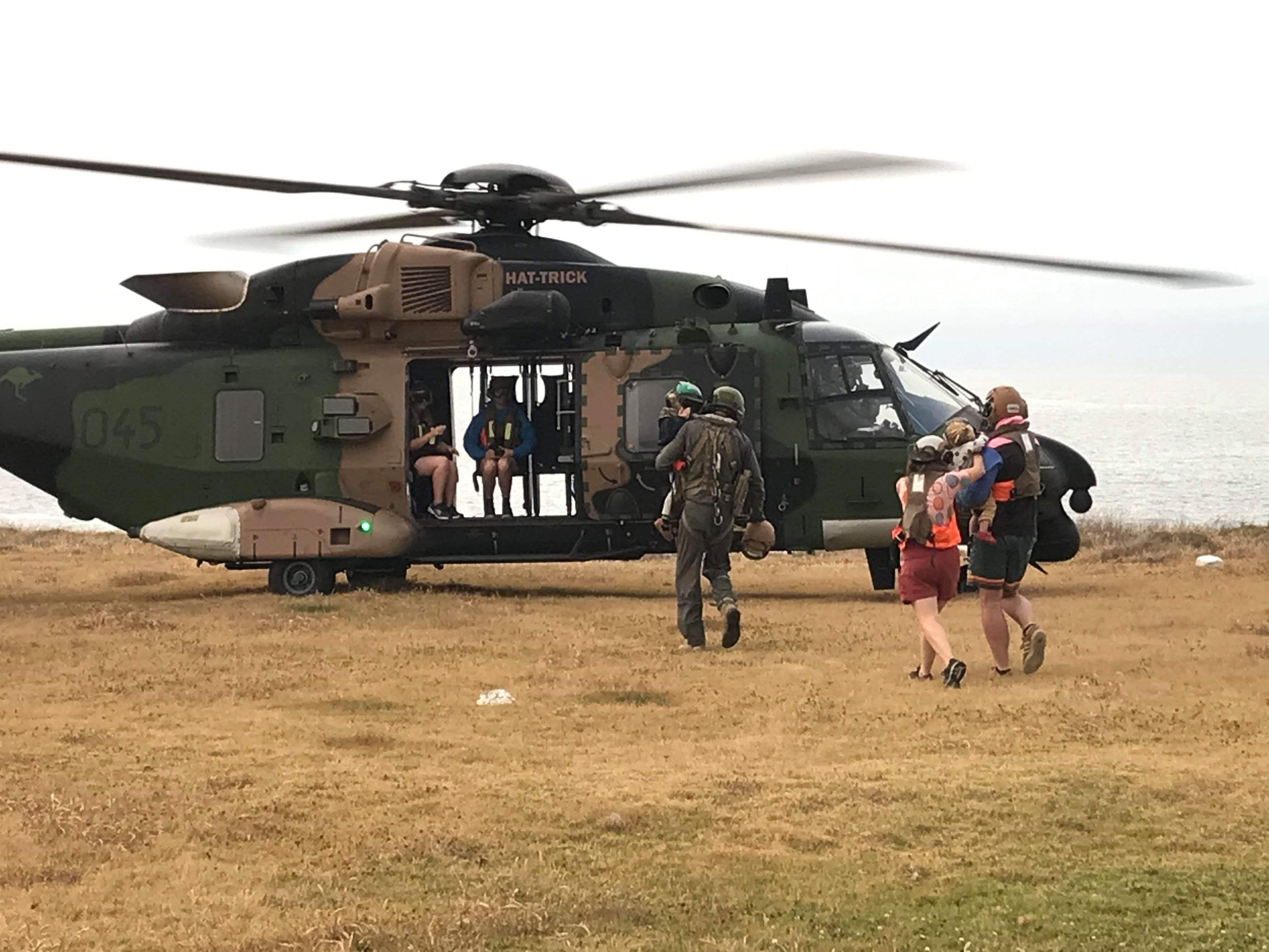Image of a navy helicopter with people running towards it, the water in the background. 