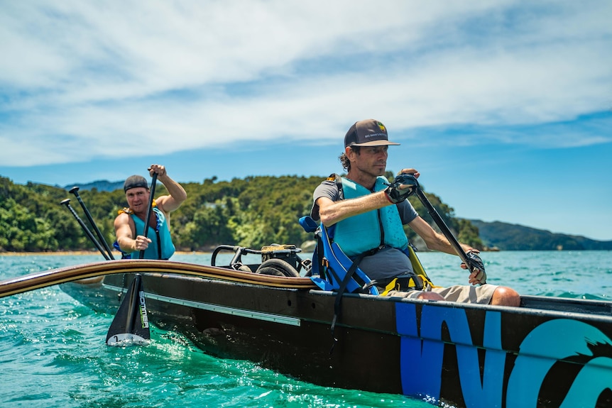 Two men in a kayak on blue water on a sunny blue sky day