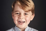 Prince George, wearing a striped shirt with its top button undone, smiles for an official portrait.