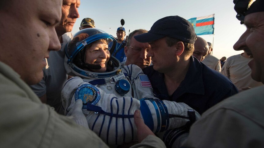 A crowd helps astronaut Peggy Whitson out of her spacecraft.