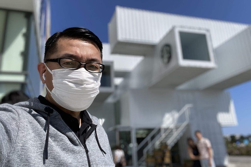 Vincent Hsu looks at the camera wearing a mask, it looks like he's at an airport.