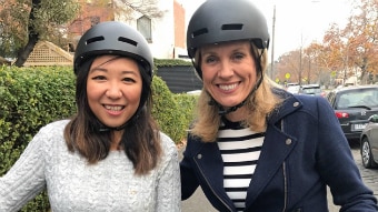 Two women wearing bike helmets on a suburban street.