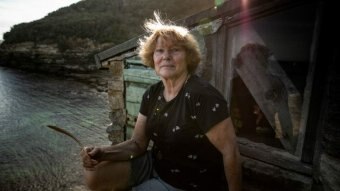 A woman sitting in front of a small building looks at the camera