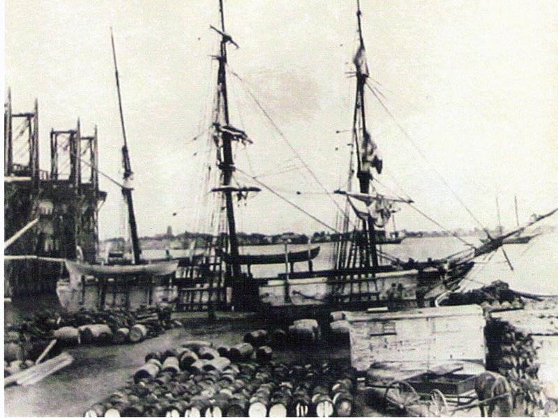 A three-masted whaling ship, the Catalpa, with barrels of whale oil in the foreground.