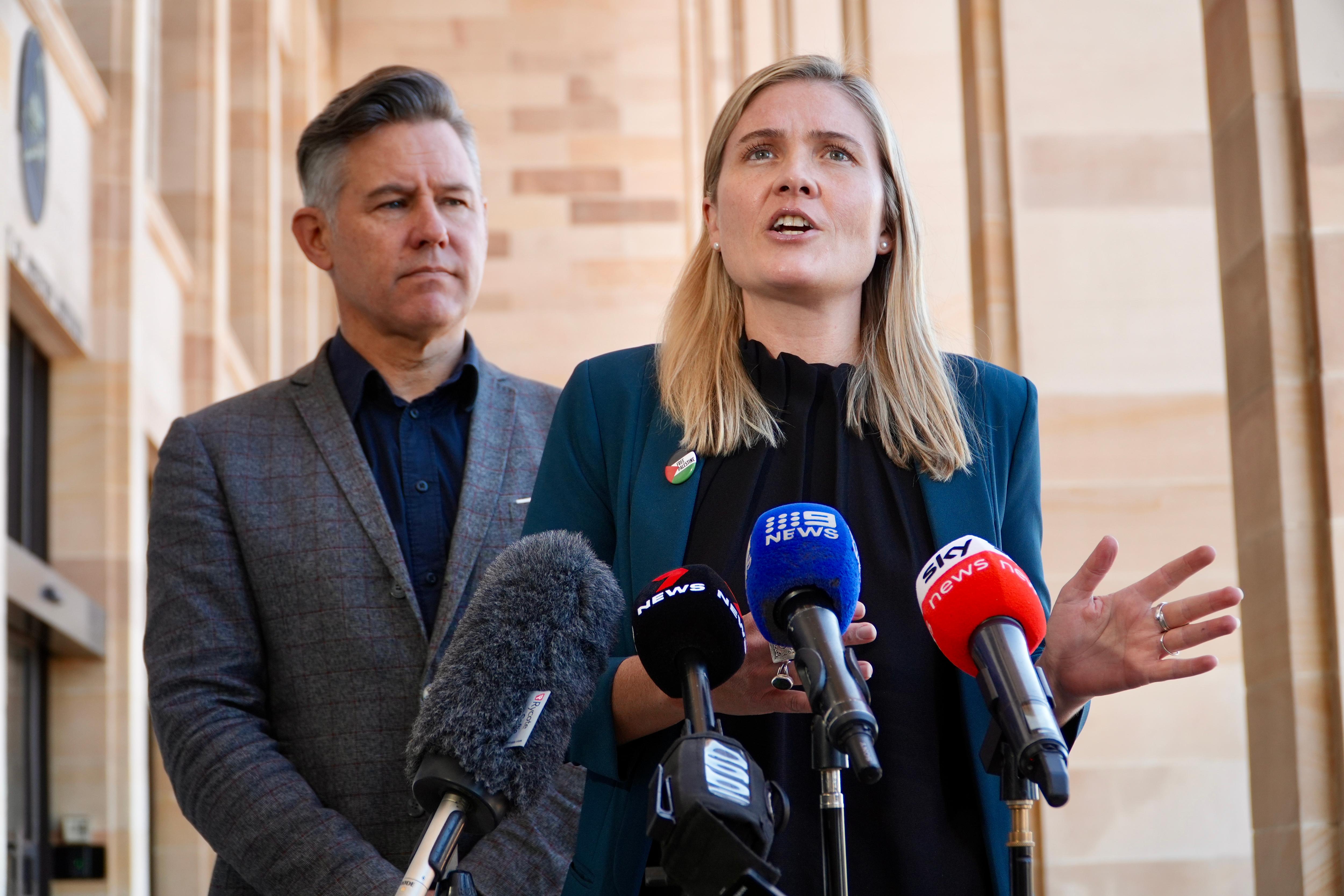 A woman speaks at a lectern as a man watches on.