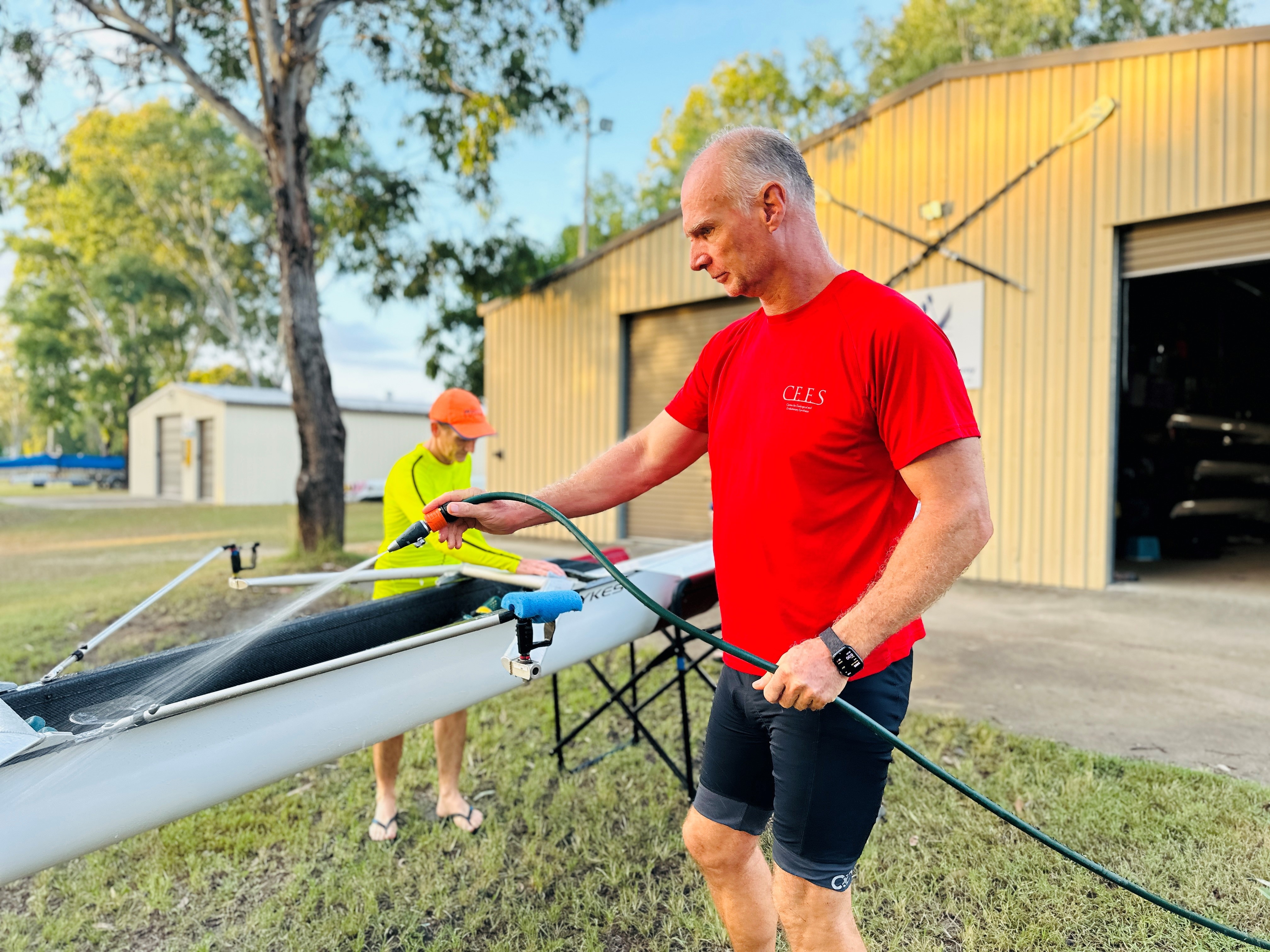 Two men hosing and cleaning a rowing boat.