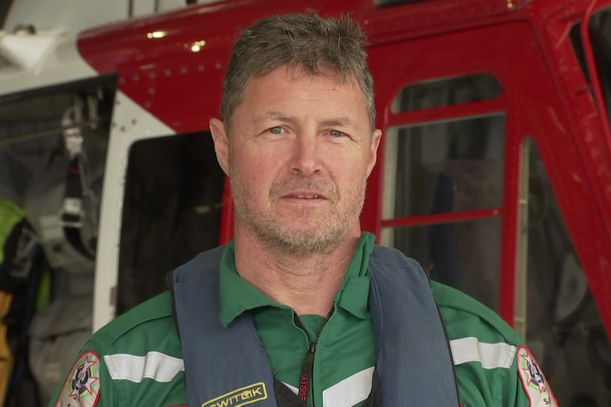 A man looking directly at the camera wearing a green paramedic uniform