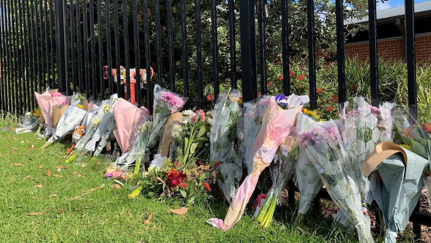 Bunches of bright flowers resting against a fence of Ulladulla High School July 2020