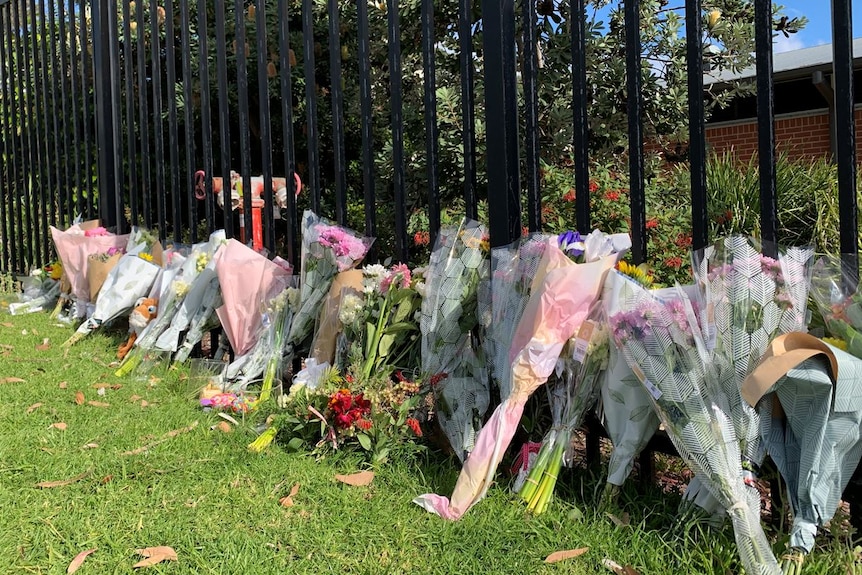 Bunches of bright flowers resting against a fence of Ulladulla High School July 2020