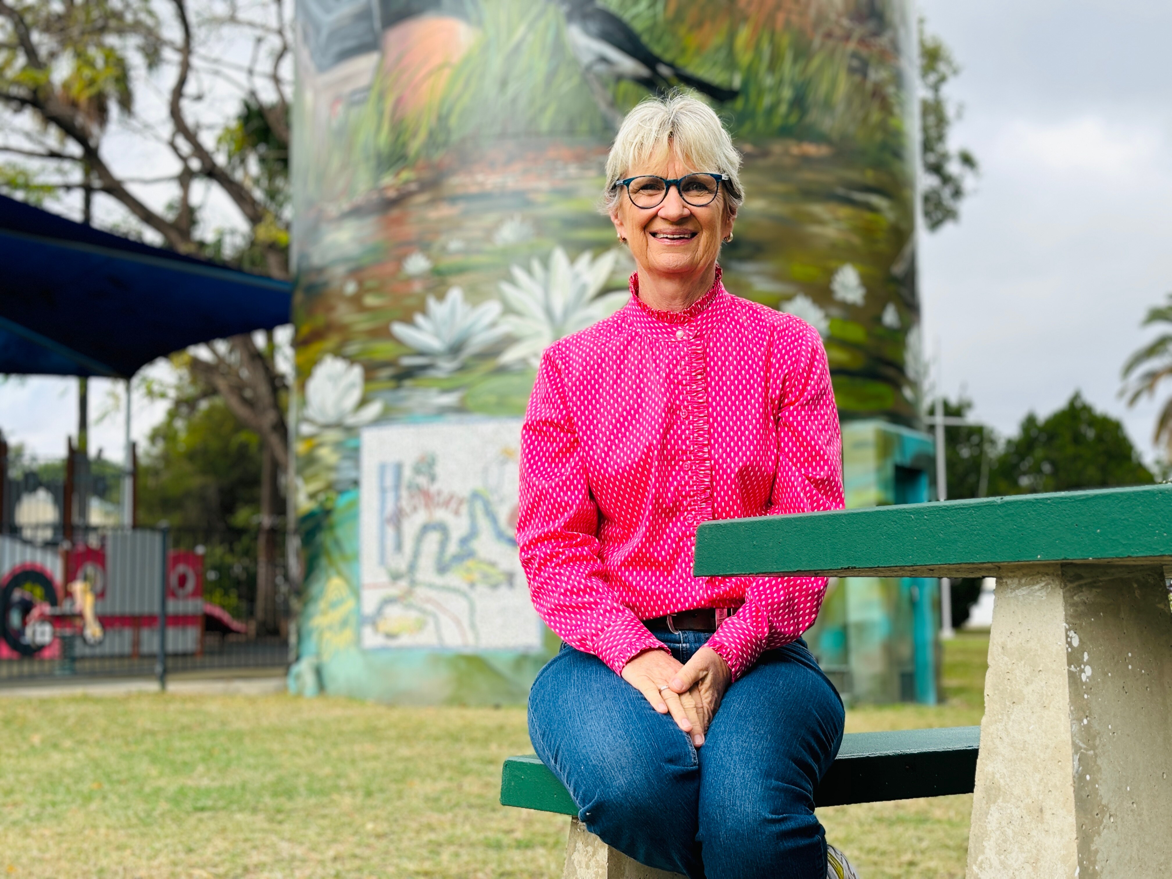Woman in a pink shirt is sitting in front of a water tower.