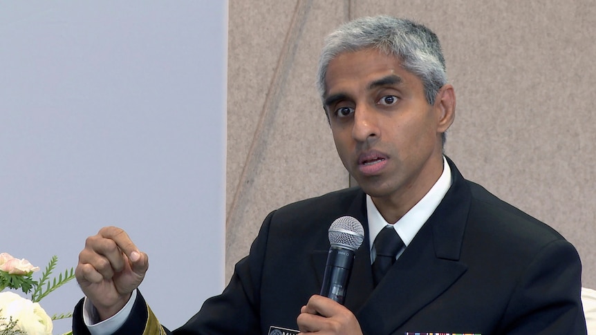 A man wearing a black suit jacket with military medals and speaking into a microphone