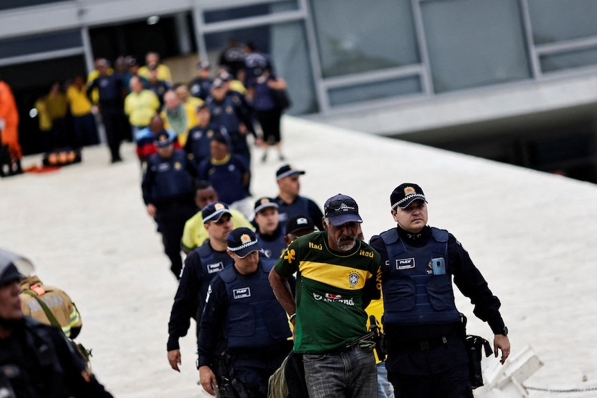 Police march protesters in handcufs down a white ramp. 