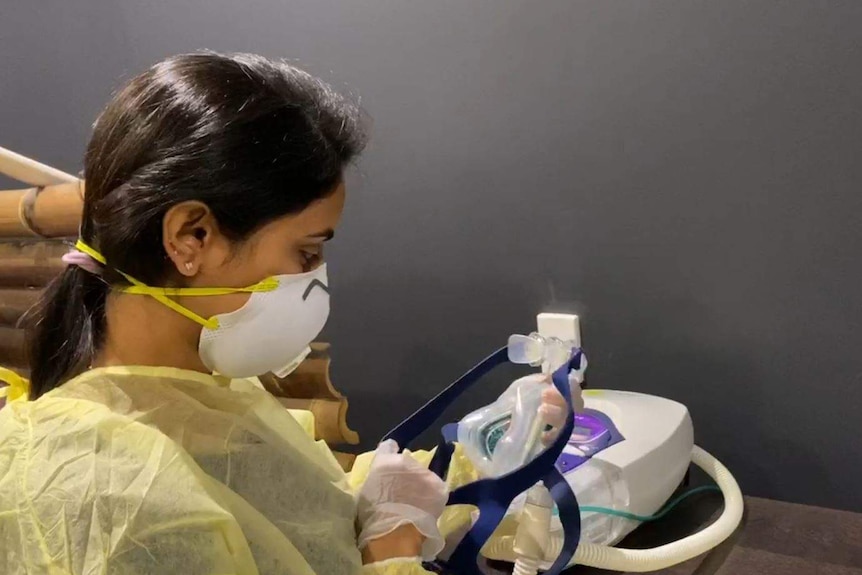 A woman wearing a mask, gown and gloves handling a ventilation mask.