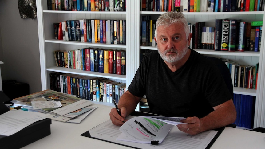 Peter Gogarty sits at a desk with papers and a pen in his hands looking at the camera.