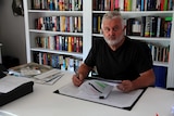 Peter Gogarty sits at a desk with papers and a pen in his hands looking at the camera.